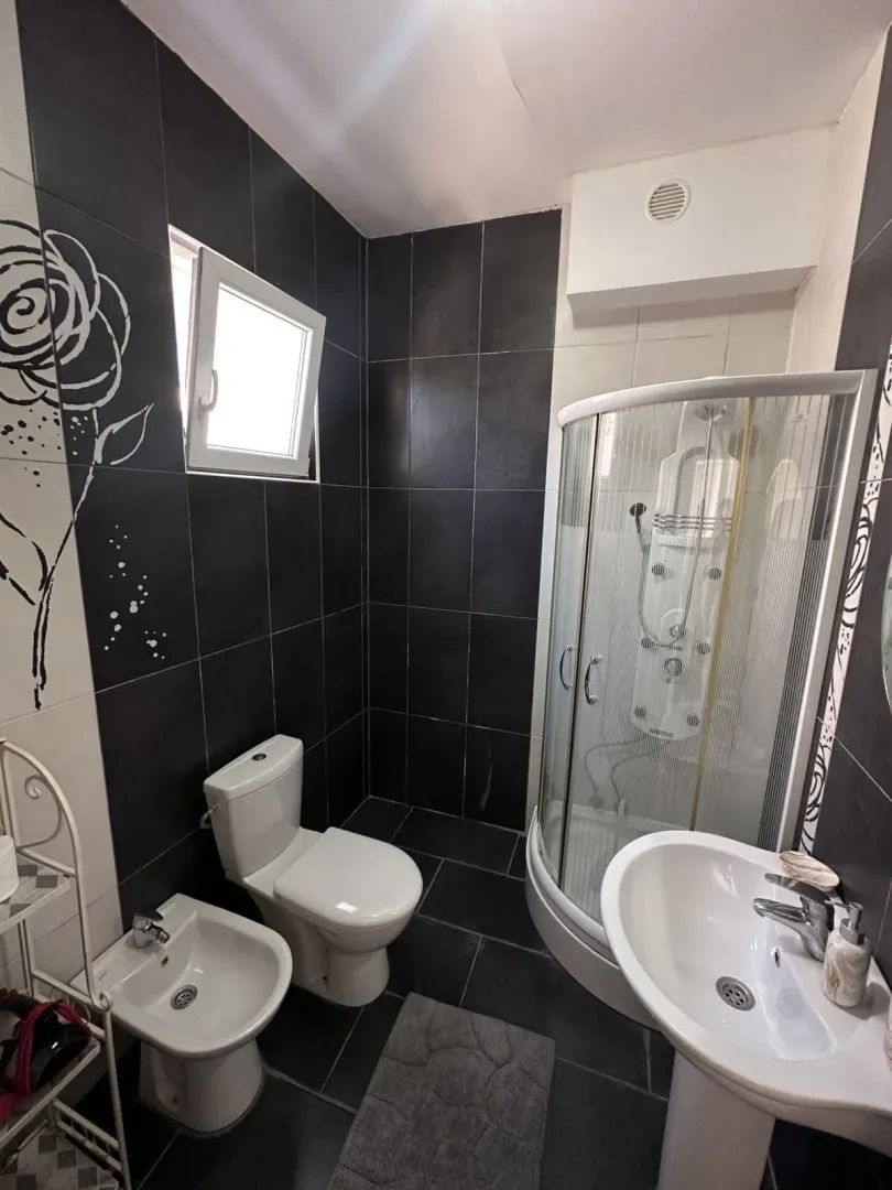 Savremeno opremljeno kupatilo sa tuš kabinom i crnim pločicama.