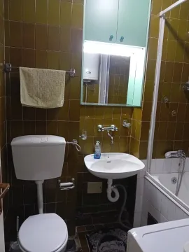 Kupatilo sa smeđim pločicama, lavaboom i kadom. - image 10