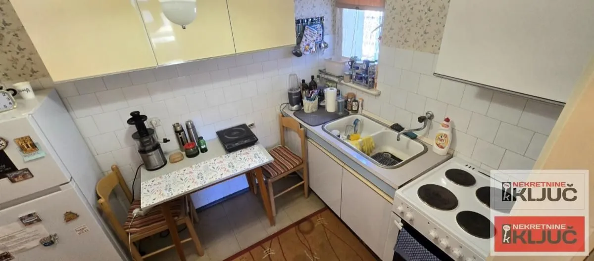 Manja kuhinja sa elementima, šporetom i trpezarijskim stolom sa stolicama.