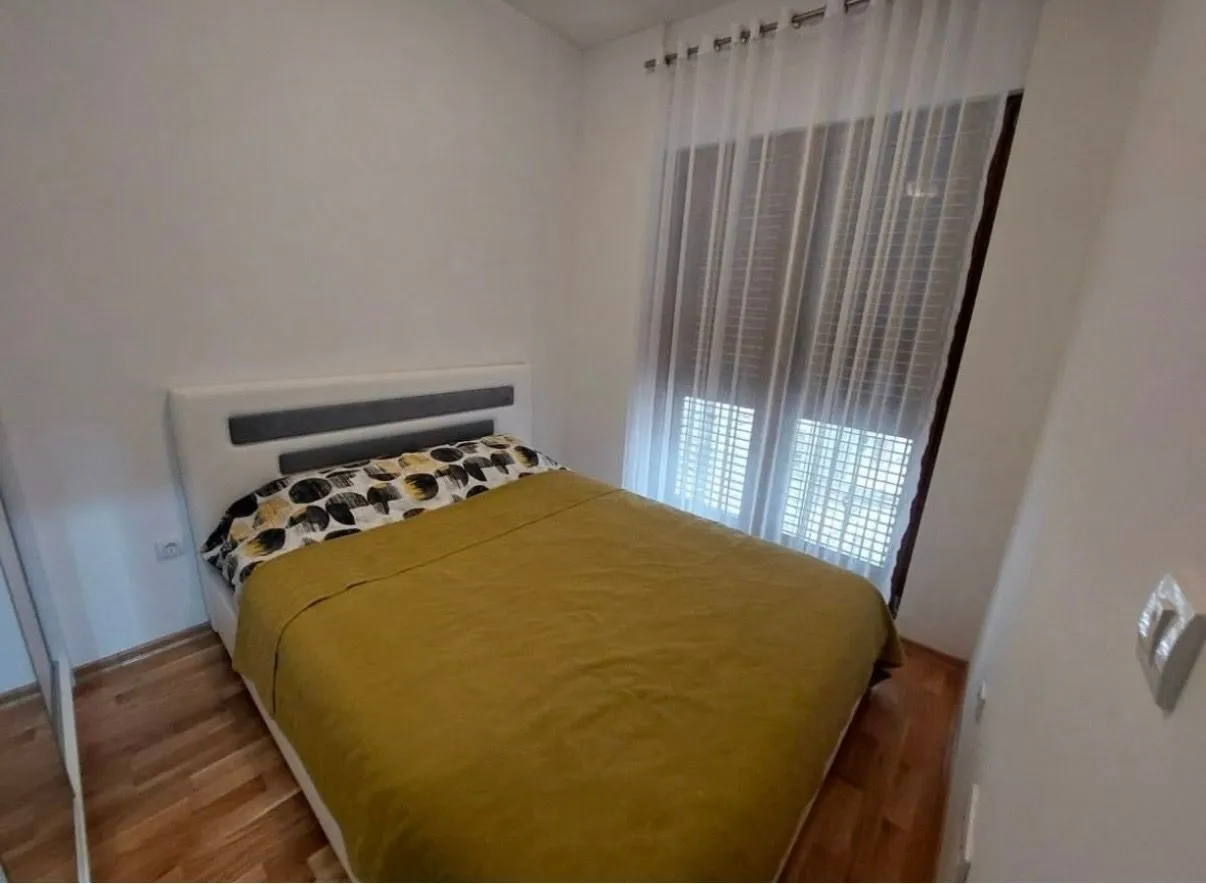 Uređena spavaća soba sa bračnim krevetom i prozorom sa zavjesama.
