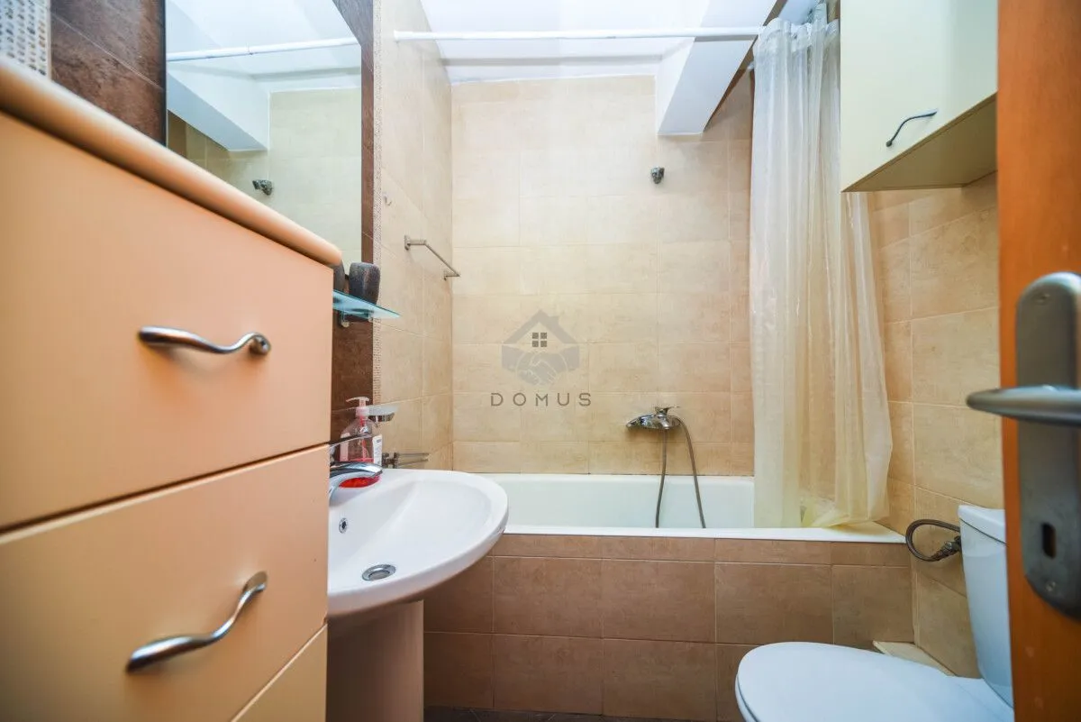 Small bathroom tiled in beige with a bathtub, washbasin, and toilet.