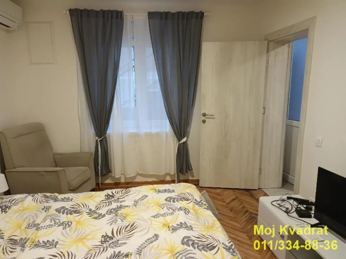 Furnished bedroom with a bed, armchair, and a window with curtains.
