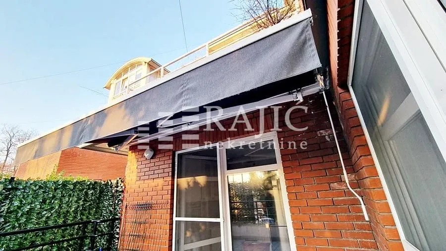 Spoljašnji deo kuće sa ciglenom fasadom, balkonom i tendom.
