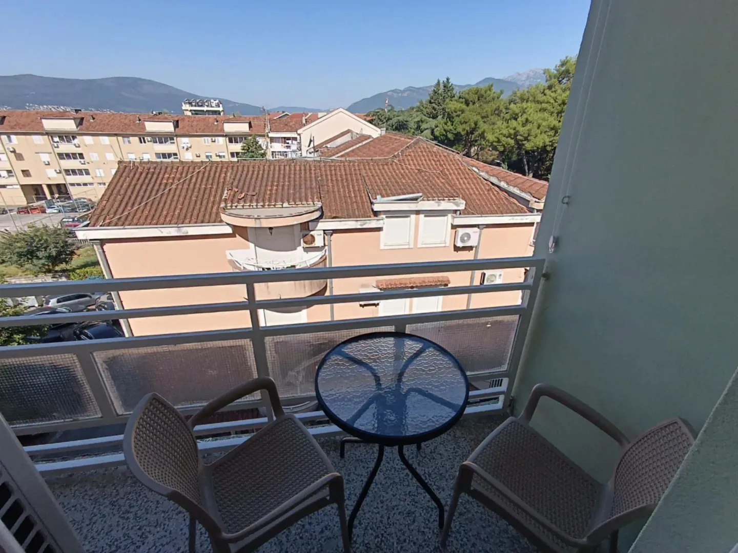 Namješten balkon sa stolom i dvije stolice i pogledom na okolne zgrade i brda.