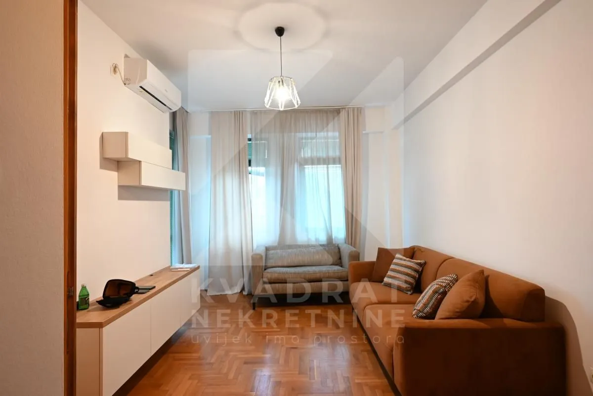 Living room with a brown sofa, a smaller grey sofa, parquet flooring, and an air conditioner.