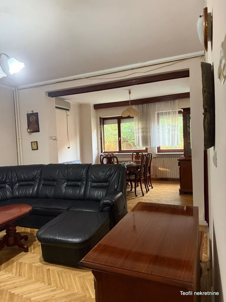 Dnevna soba sa crnom kožnom garniturom i pogledom na trpezariju u pozadini.