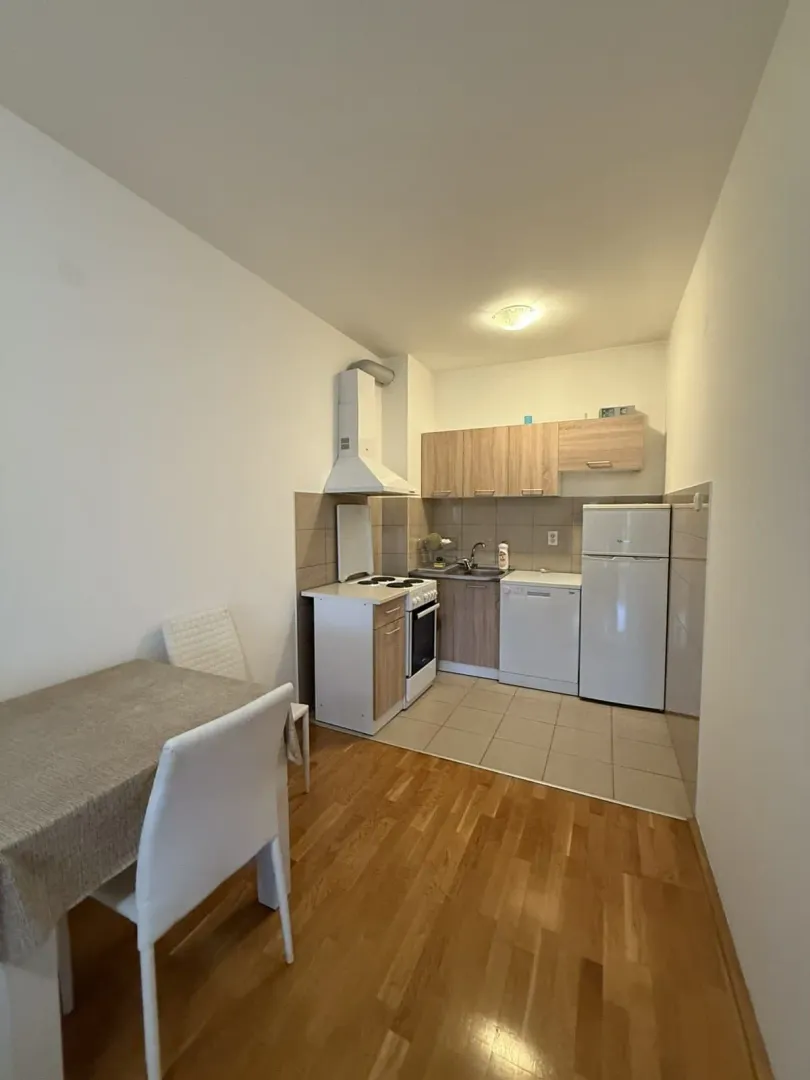 Compact kitchen with wooden cabinetry, sink, stove, refrigerator, and a dining table.