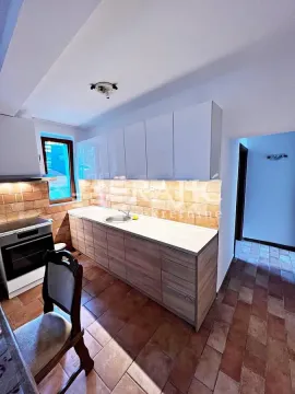 View of the kitchen with wooden cabinets, white wall units and a dining chair in the foreground. - image 9
