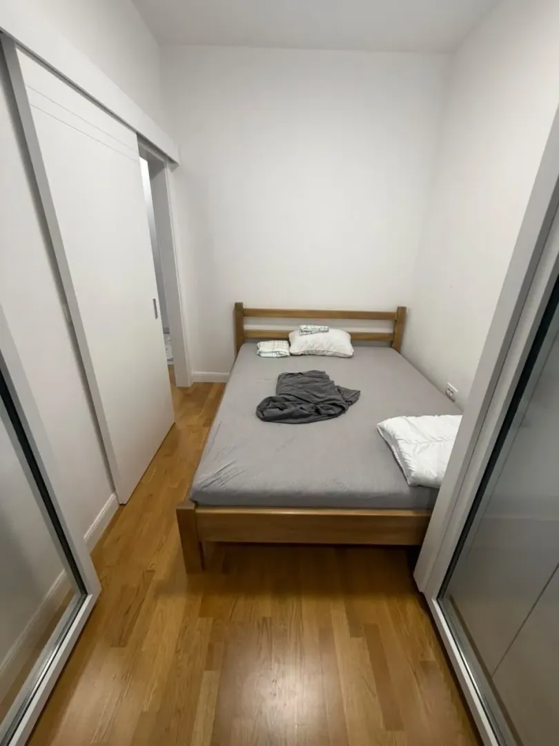 Manja spavaća soba sa bračnim krevetom i drvenim podom.