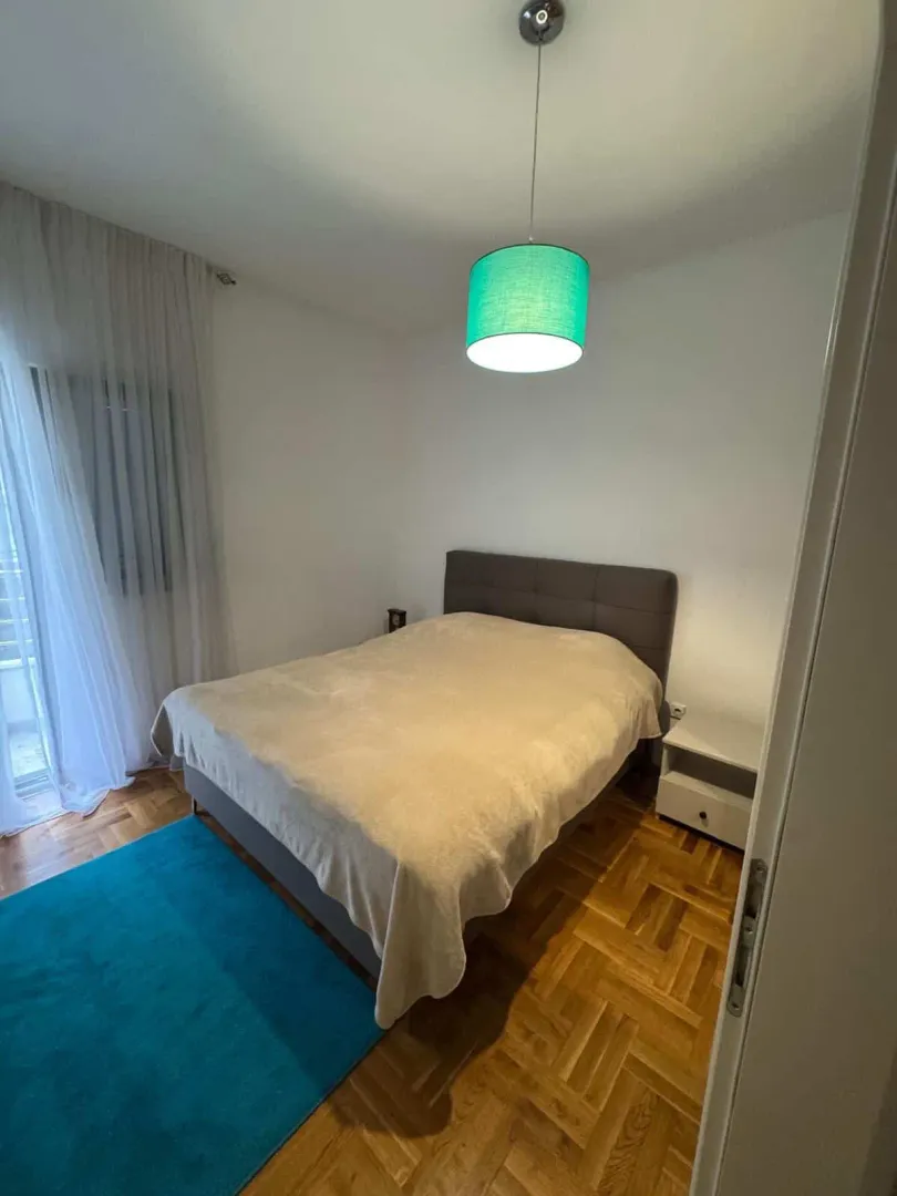 Uređena spavaća soba sa bračnim krevetom, parketom i zelenom visućom lampom.