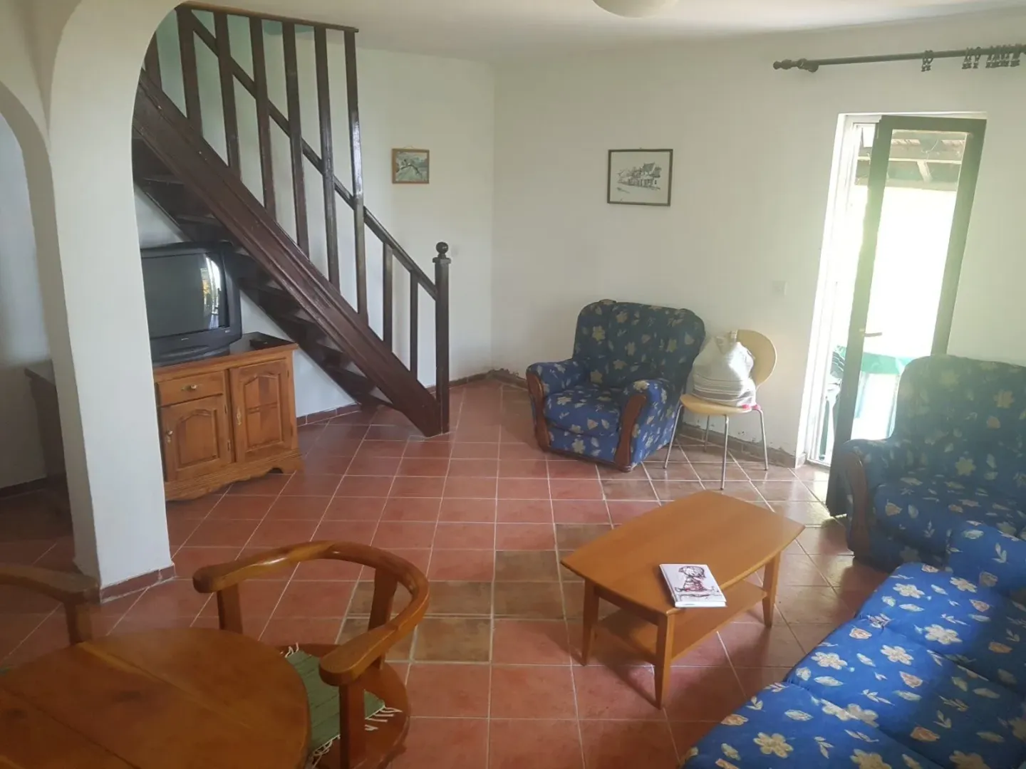 Spacious living room with sofa set, wooden staircase and ceramic floor tiles.
