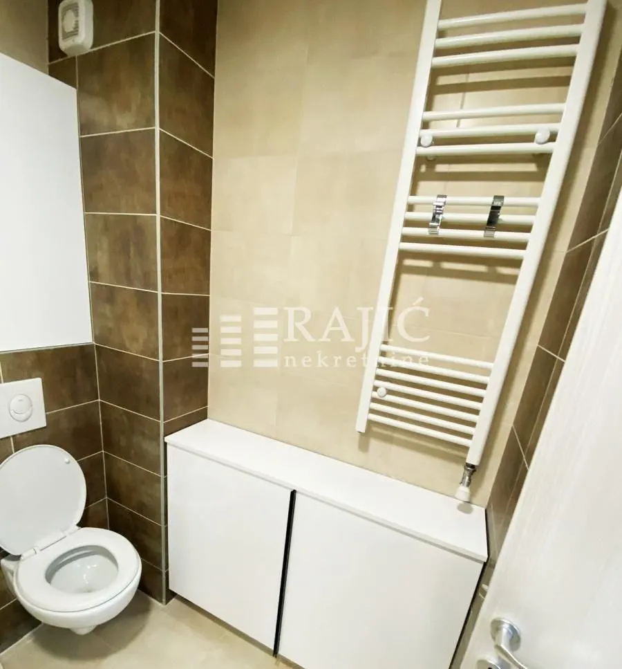 View of the bathroom with a toilet, white cabinet, and towel rail radiator.
