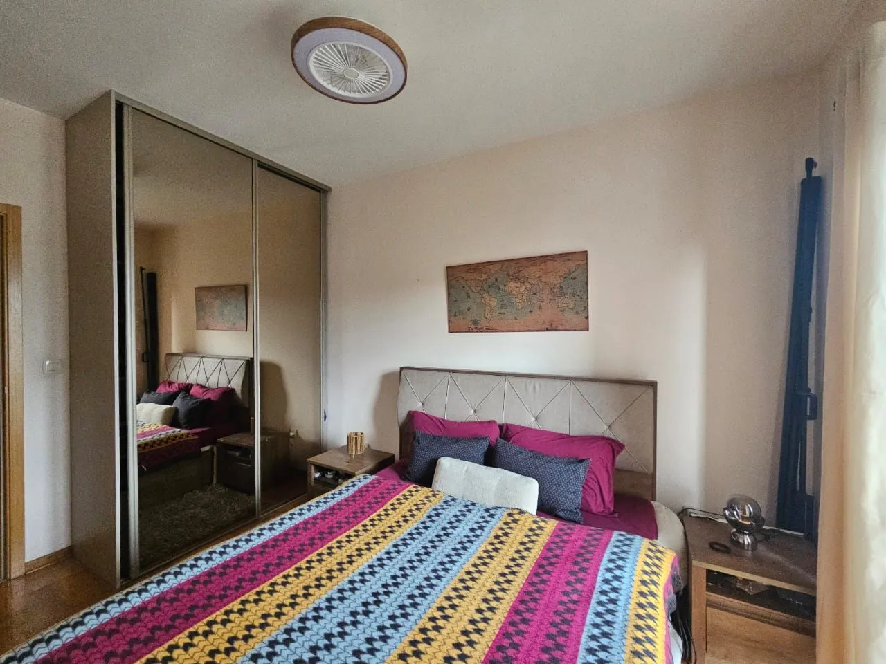 Spavaća soba sa bračnim krevetom, noćnim stočićima i velikim plakarom sa ogledalom.