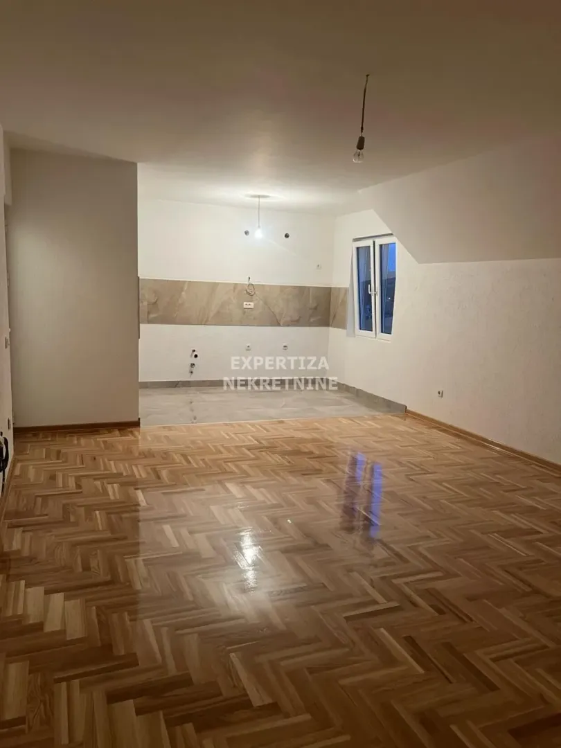 Spacious empty room with parquet flooring and a tiled kitchen area.