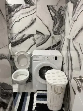 Bathroom equipped with a toilet, washing machine, and laundry basket. - image 5