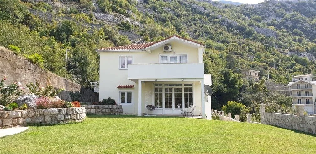 A two-story house with a landscaped lawn set against a mountain background.