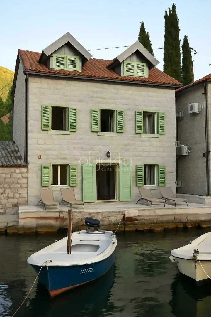 Pogled na eksterijer tradicionalne kamene kuće na obali mora sa čamcem u prvom planu.