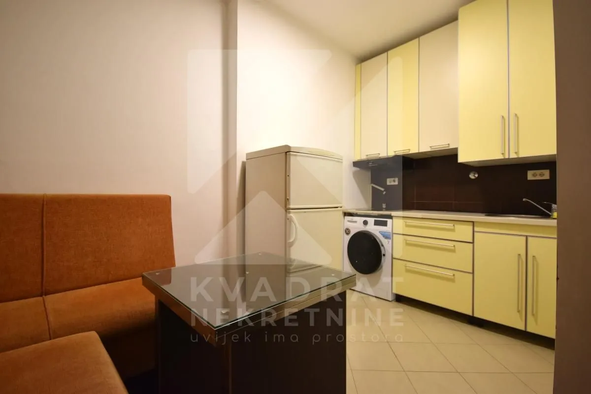 Manja kuhinja sa žutim elementima, frižiderom i veš mašinom u nastavku.