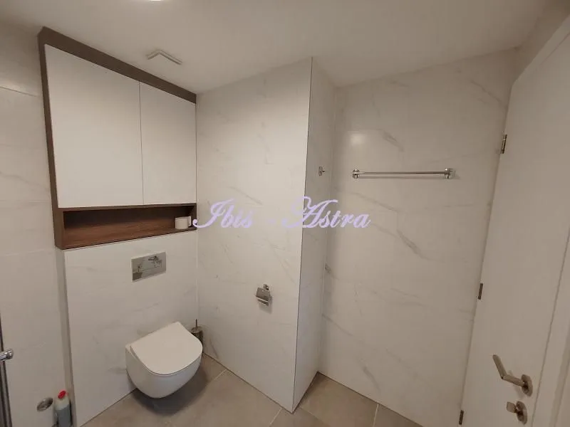 Modern bathroom with white tiles and a wall-mounted toilet.