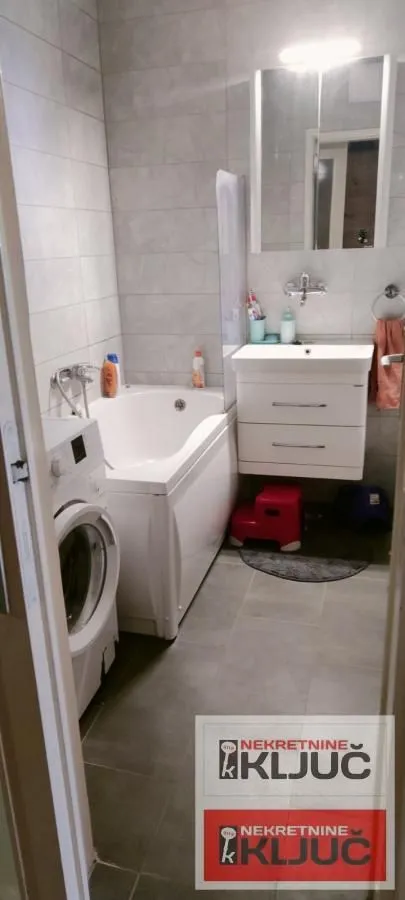 Kupatilo opremljeno kadom, umivaonikom, ogledalom i veš mašinom.