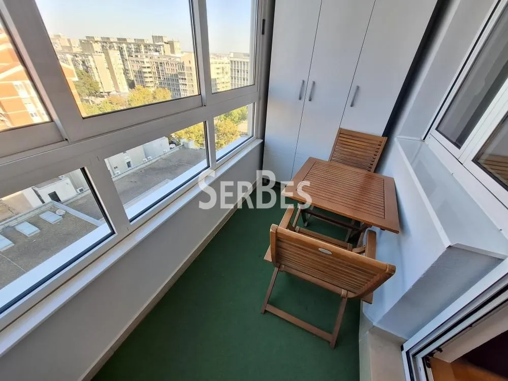 Zastakljeni balkon sa drvenim stolom, stolicama i ugradnim ormanom.