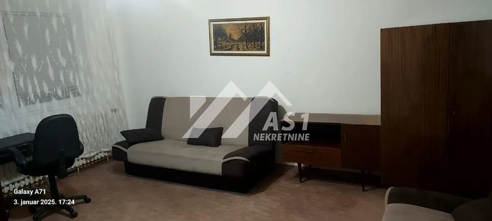 Dnevna soba sa kaučem, foteljom, radnim stolom i drvenim ormarima.