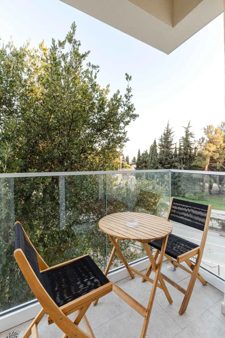 Namješten balkon sa drvenim stolom i stolicama i pogledom na zelenilo.