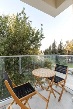 Namješten balkon sa drvenim stolom i stolicama i pogledom na zelenilo. - image 18