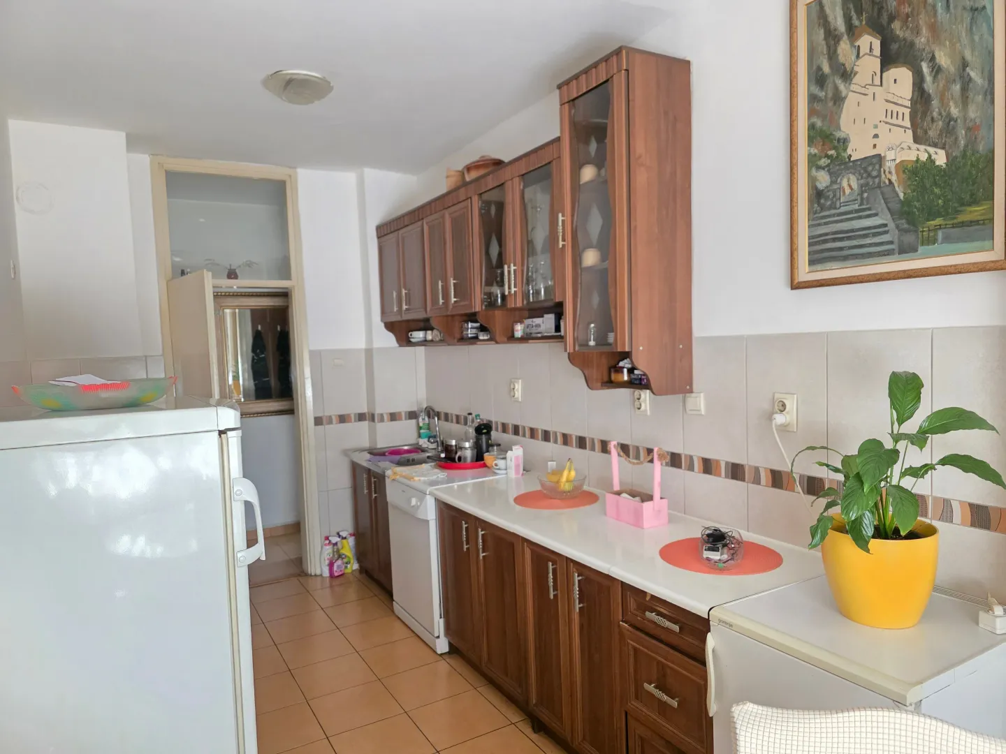 Kuhinja sa drvenim elementima i bijelom radnom površinom.