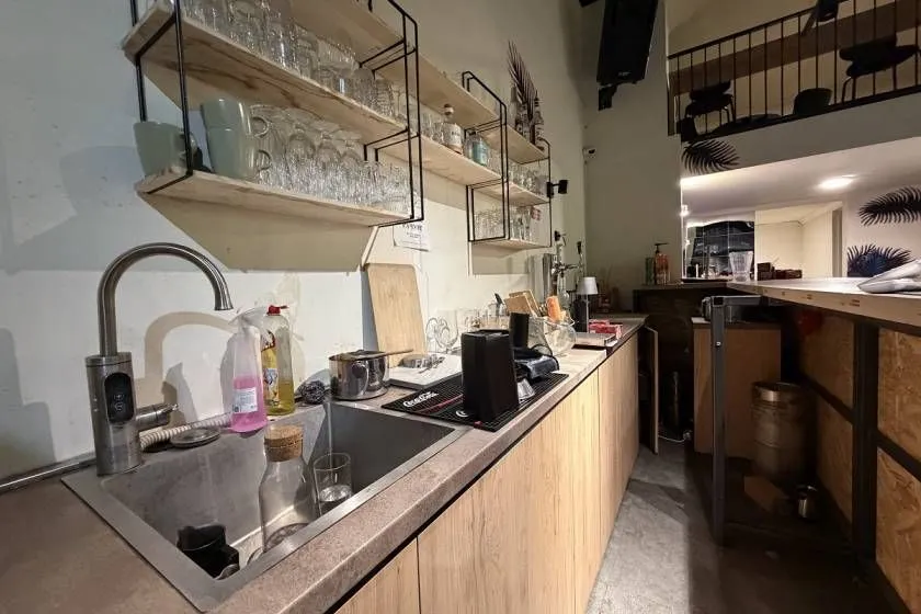 Kitchen area with a sink, countertop, and glass shelving on the wall.