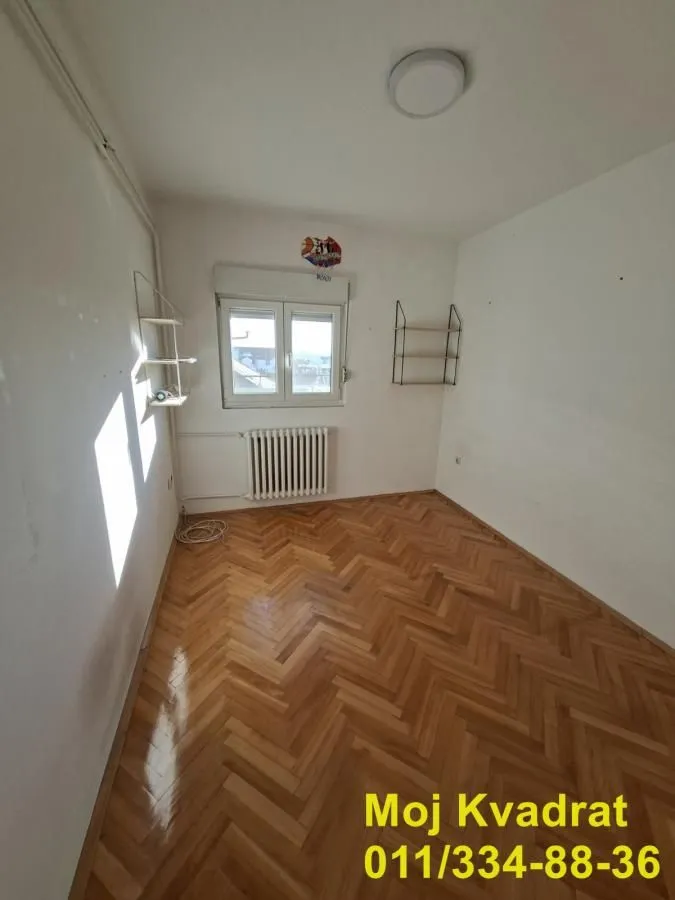 Empty room with wooden parquet flooring and a window.