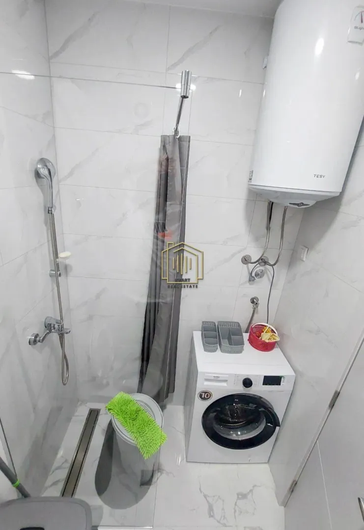 Smaller bathroom with a shower enclosure, toilet, water heater, and washing machine.