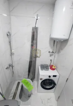 Smaller bathroom with a shower enclosure, toilet, water heater, and washing machine. - image 4
