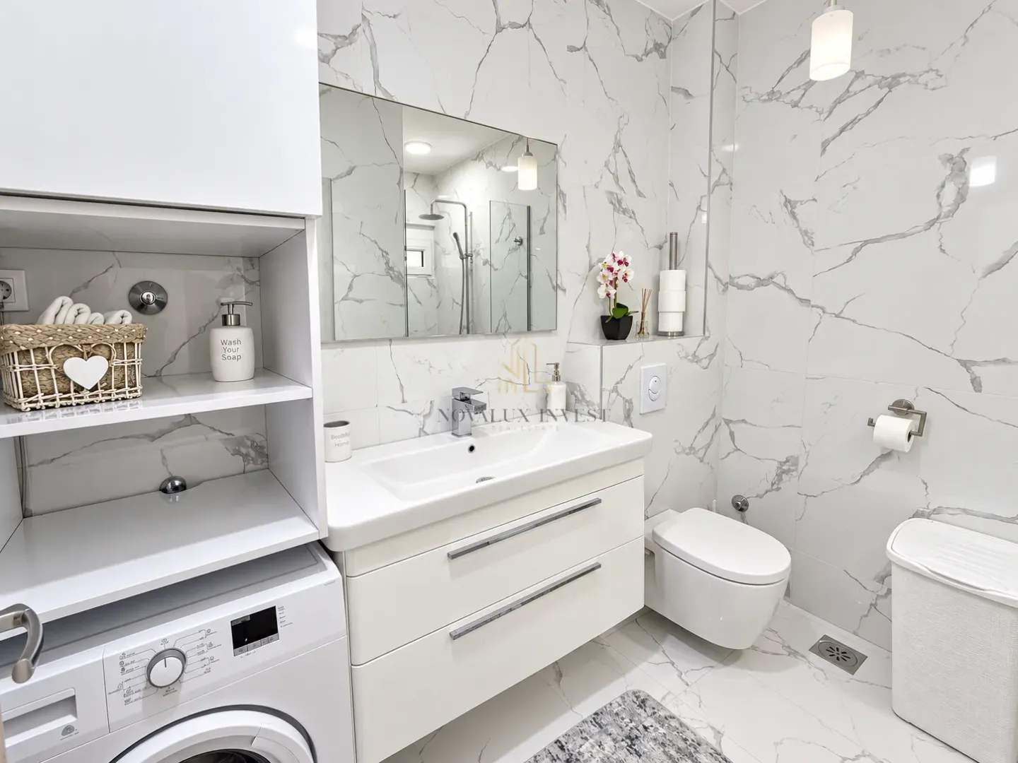 Modern bathroom with white marble tiles, vanity unit, and integrated washing machine.