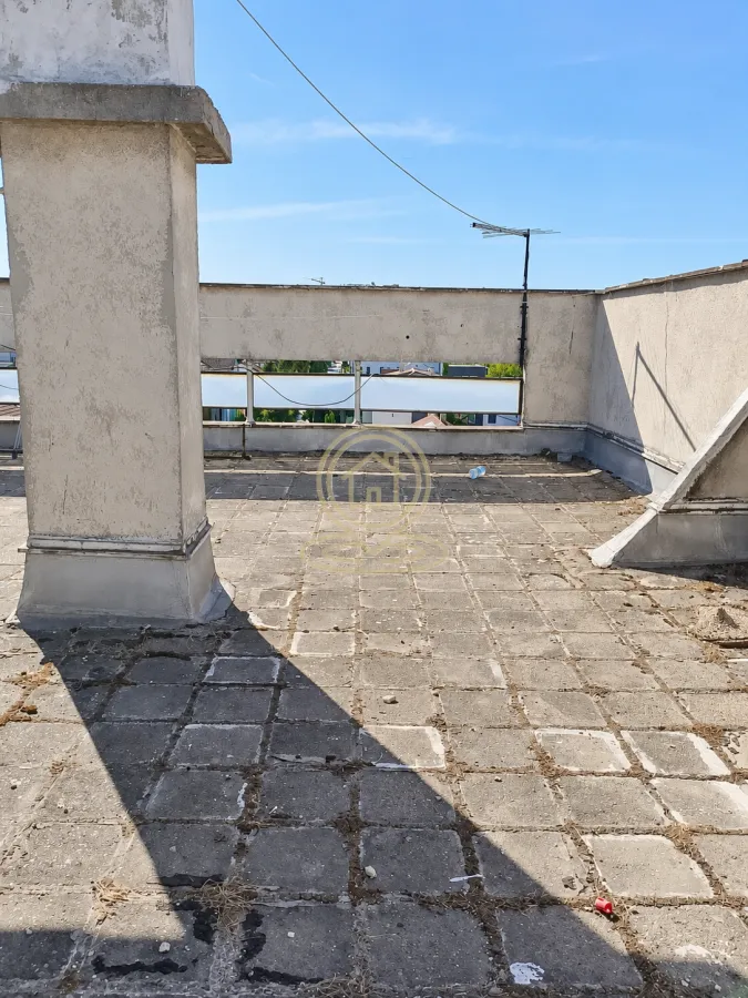 Prostrana krovna terasa sa popločanim podom i niskim zidom.