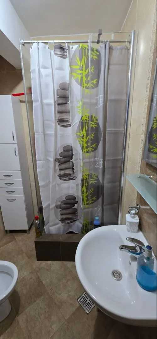 Manje kupatilo sa umivaonikom, tuš kabinom i bijelim ormarićem.