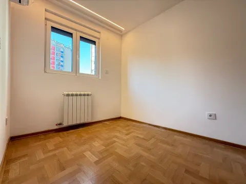 Prazna soba sa parketom, belim zidovima i radijatorom ispod prozora. - image 9