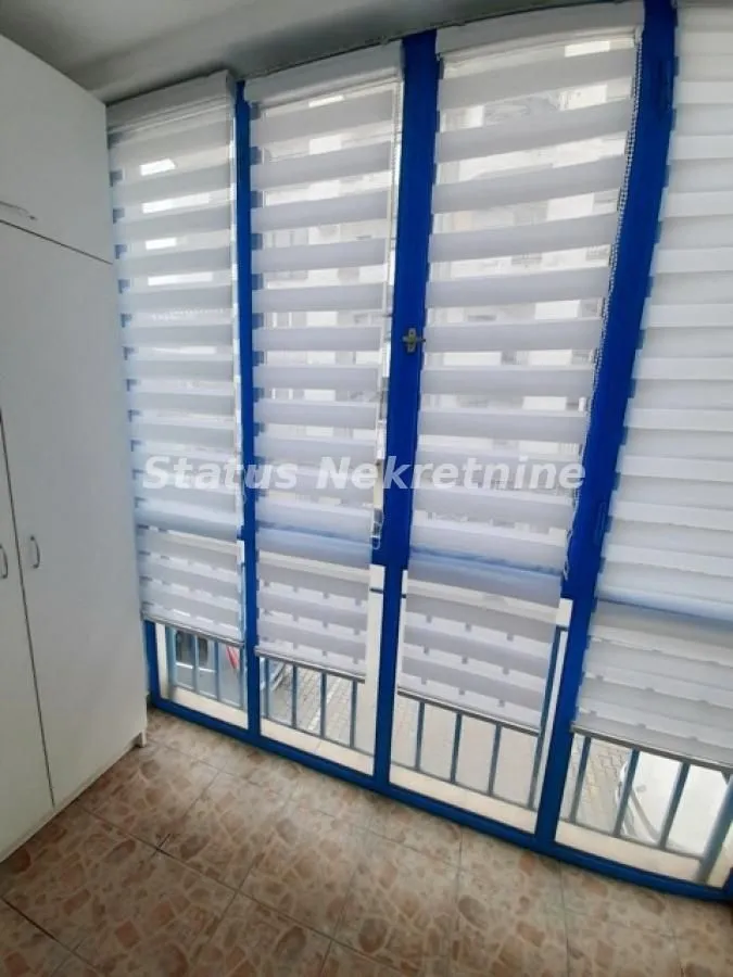 Zastakljeni balkon sa roletnama na prozorima i keramičkim pločicama na podu.