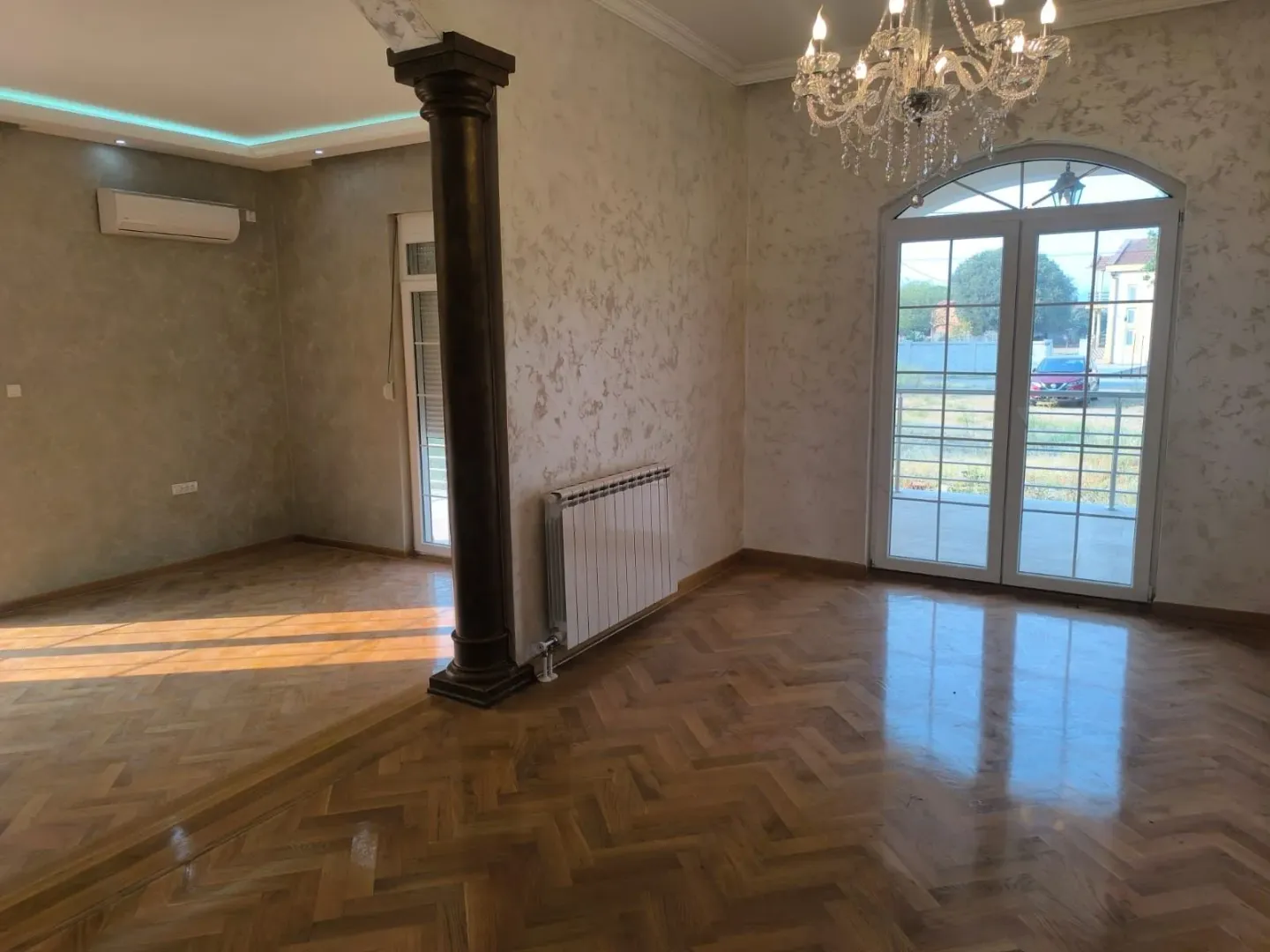 Spacious empty living room with parquet flooring and a decorative pillar.