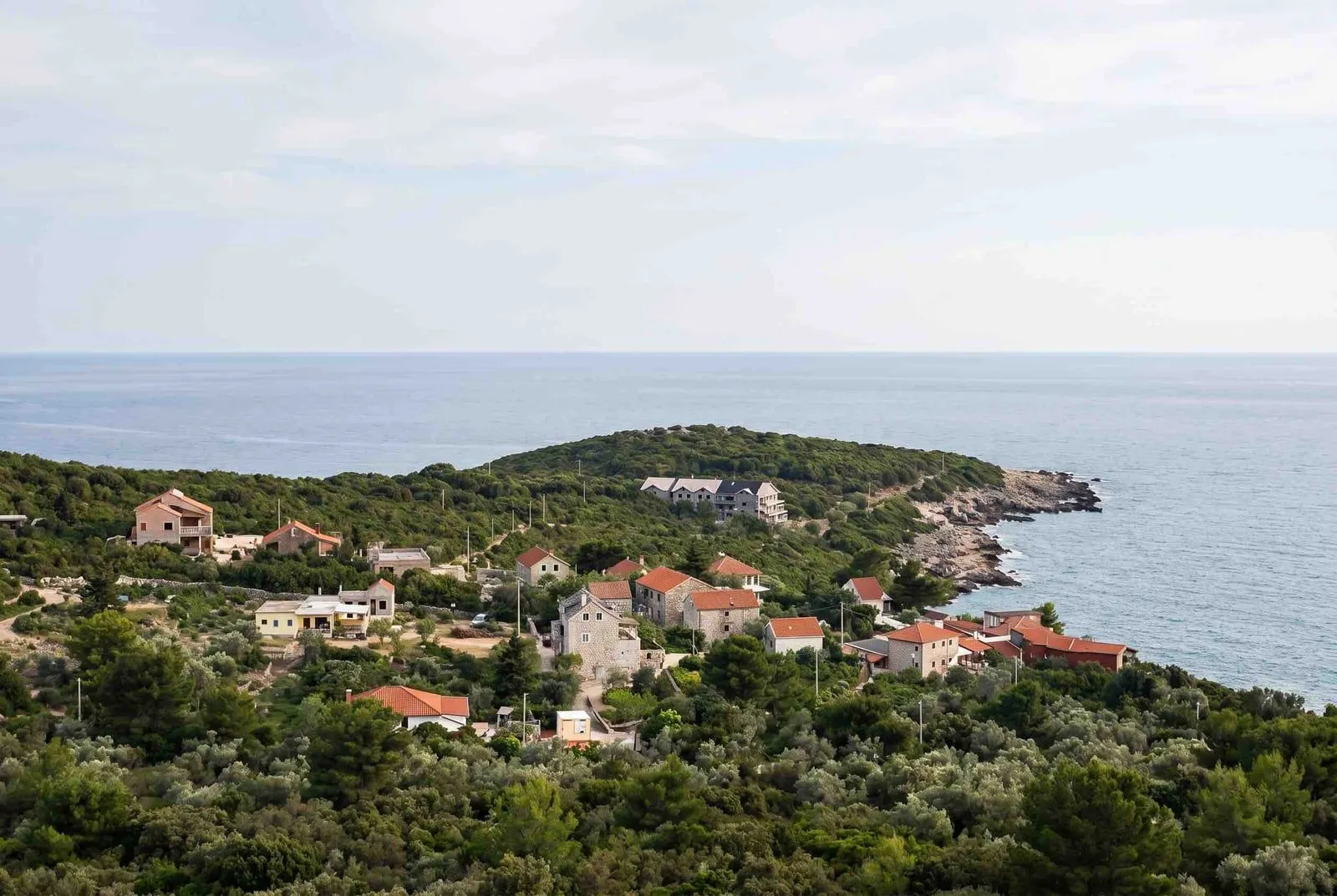 Pogled na primorsko naselje sa kućama okruženim zelenilom i morem.