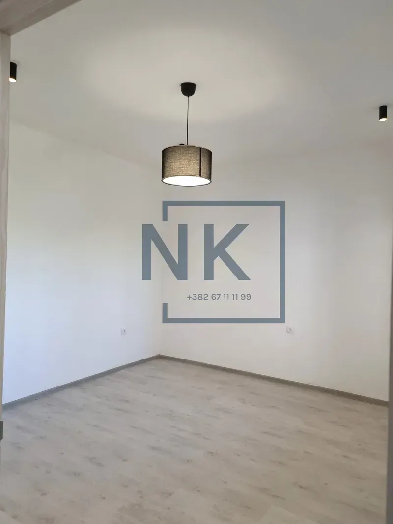 Empty room with white walls, laminate flooring, and a ceiling pendant light.