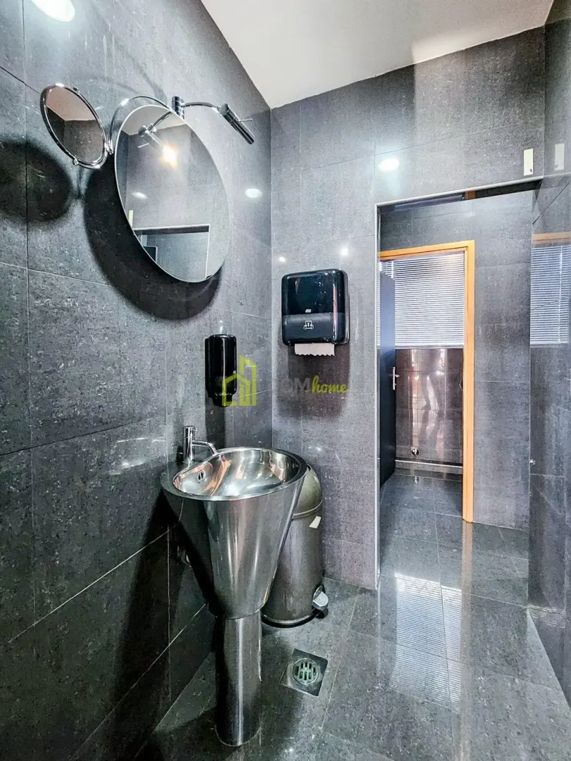 Modern bathroom equipped with dark tiles, a washbasin, and a round mirror.