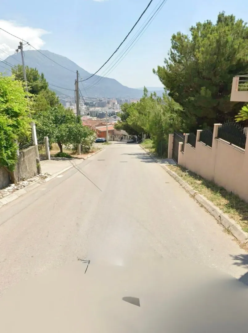Pogled na ulicu i okolno naselje sa brdima u pozadini.
