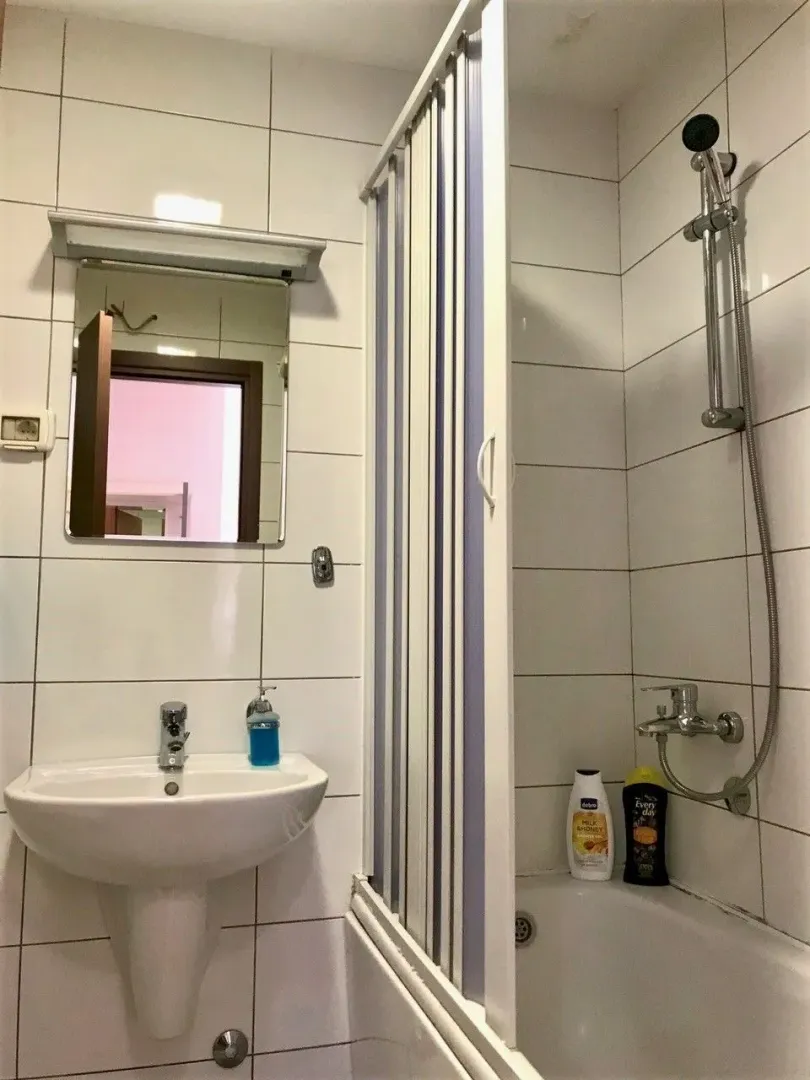 Jednostavno kupatilo sa kadom, tušem i umivaonikom sa ogledalom.