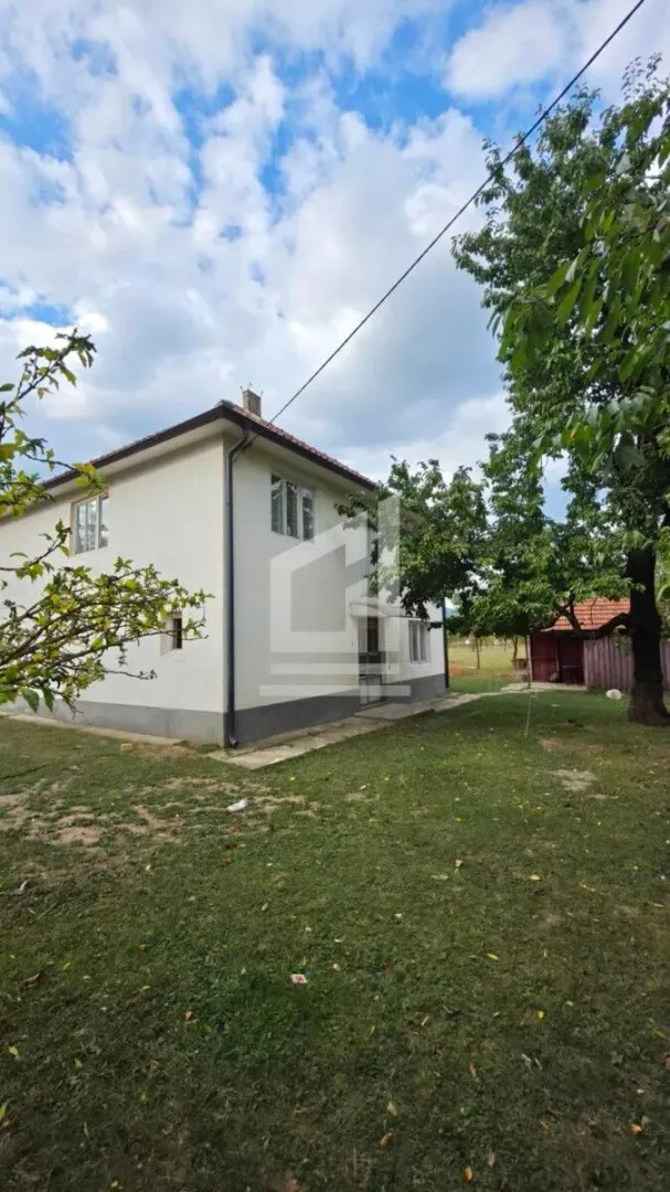 Pogled na dvorište i spoljašnjost kuće sa zelenom površinom i drvećem.