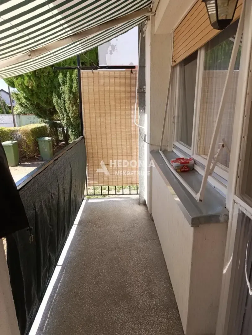 Pogled na natkriveni balkon sa zaštitom od sunca i zelenilom u pozadini.