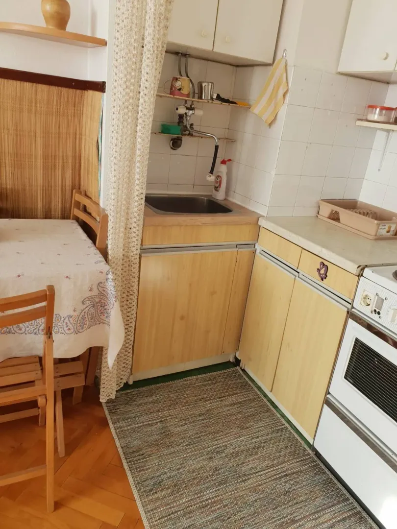 Mala funkcionalna kuhinja sa trpezarijskim stolom i drvenim elementima.