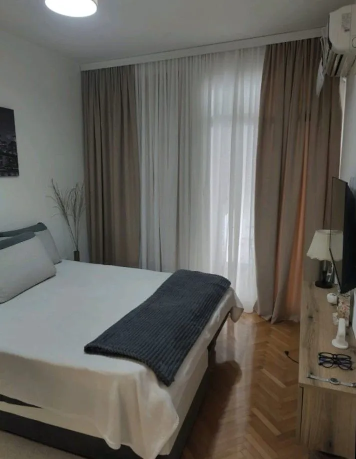 Furnished bedroom with a double bed, window, and curtains.