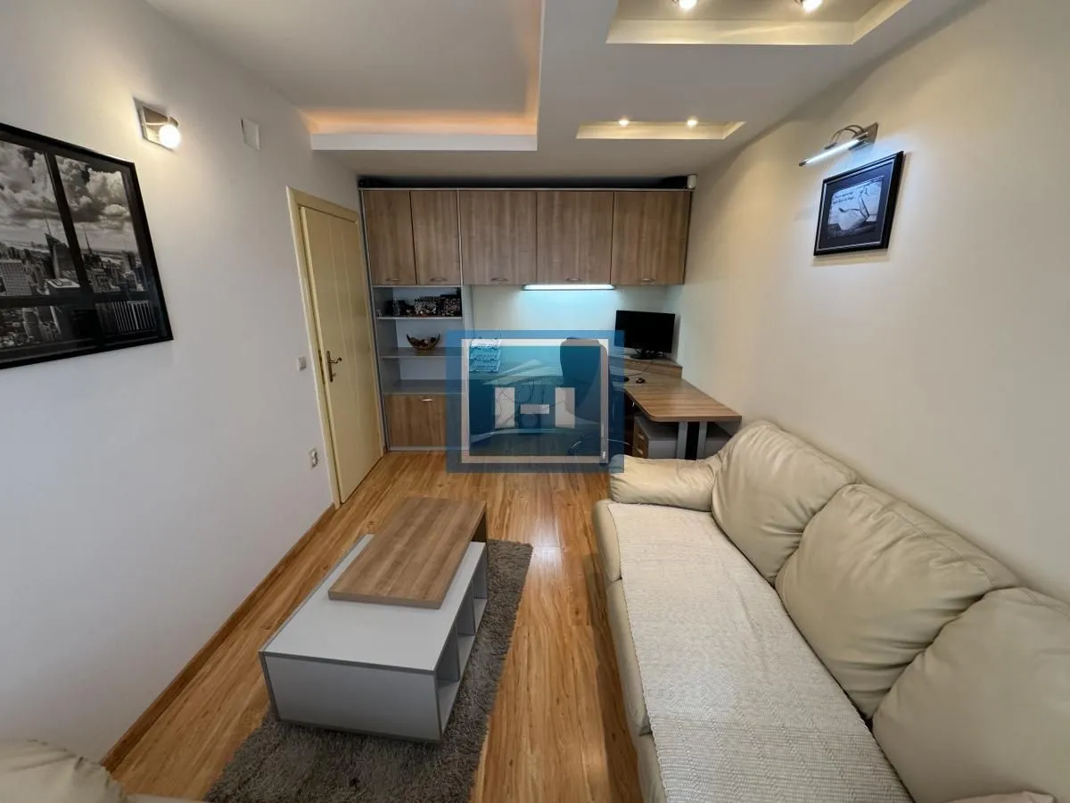 Living room with a leather sofa, coffee table, and a work area with shelving units.