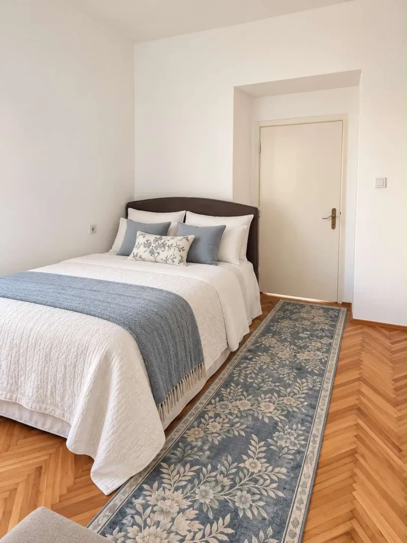 Furnished bedroom with a double bed, parquet flooring, and a rug.